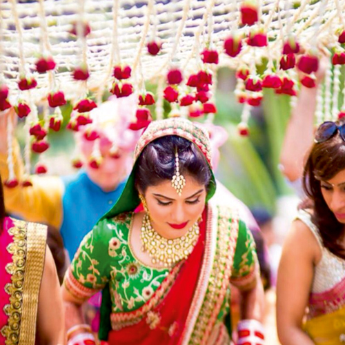 A stunning Indian bride walks alongside her friends under the flower umbrella