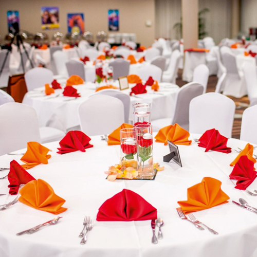 The event hall is arranged with white cloth chairs and tables, with dishes and forks for service and eating on the tables.